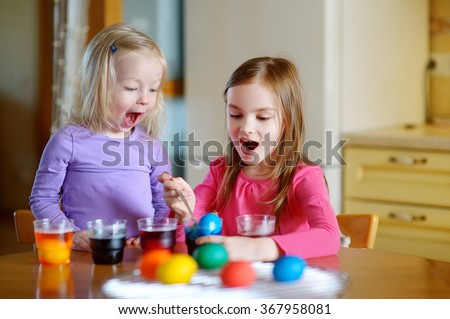 Two little sisters painting colorful Easter eggs at home
