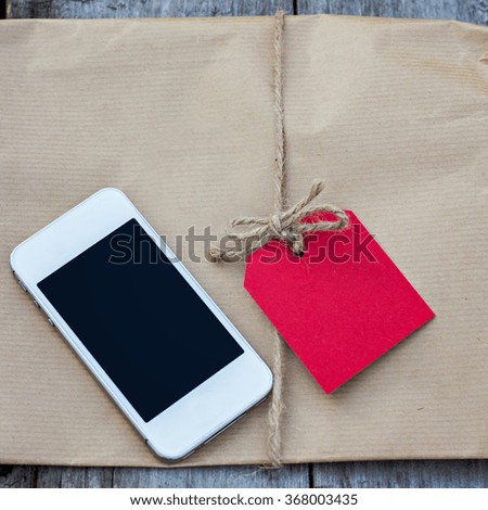 Gift in kraft paper with red card and mobile phone on a wooden table
