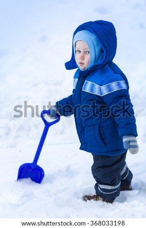 Cute baby boy playing with snow toy shovel in winter outdoor