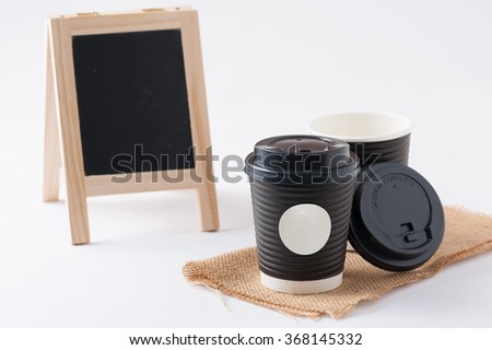 Take away paper coffee cup with white sticker label for logo, text or message and small A-frame black board in blurry background