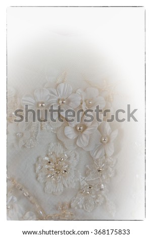 A macro photo of a detailed white wedding dress with white flowers and fake diamonds knitted to the dress with a vignet blur filter and vintage black border 
