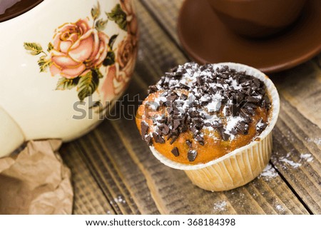 Yummy appetizing fresh baked cupcake decorated by sweet chocolate pieces food with many fats standing near beautiful teapot and brown cup on wooden background top view closeup, horizontal picture