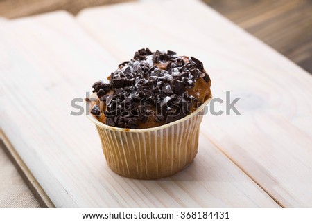 One baked fragrant fresh appetizing cupcake in paper case with chocolate fattening meal carbohydrates meal with many calories refreshment on light wooden board studio closeup, horizontal picture