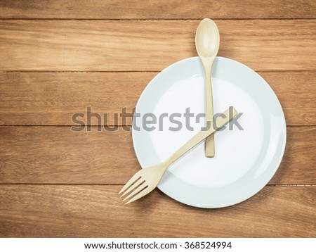 Empty white dish with wooden spoon and fork on wood table.