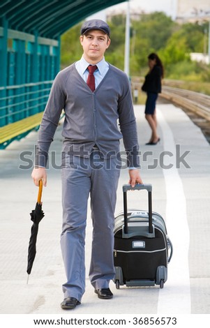 Handsome man walking down railway station with umbrella and baggage