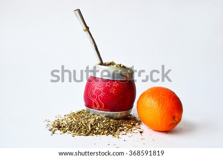 Pictured hand-made mate cup of a small pumpkin full of guarana with some spilled out. Metallic tube for drinking and a mandarin