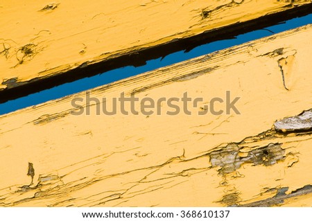 Yellow wooden planks with peeling color; Blue sky visible through a slot in wooden wall; Break walls and find new ways