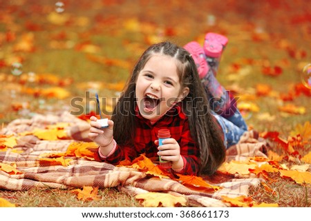 Cute girl lying on plaid and blowing soap bubbles in park