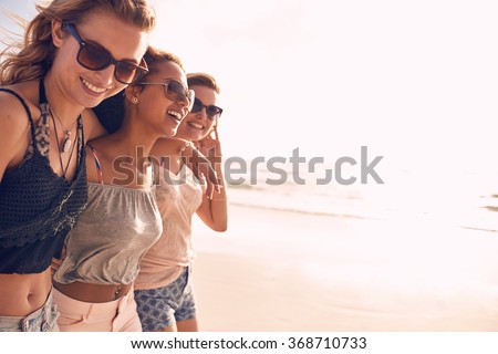 Group of beautiful young women strolling on a beach. Three friends walking on the beach and laughing on a summer day, enjoying vacation. Royalty-Free Stock Photo #368710733