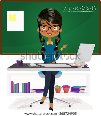 Beautiful Indian teacher, instructor at her desk with a computer by a chalkboard 