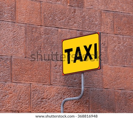 yellow TAXI sign on the taxi stop with a wall of an old building
