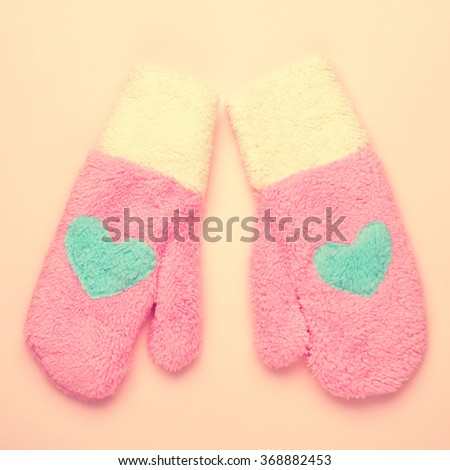 Pair of pink mittens with blue heart on pink background