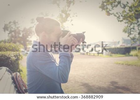 The bearded hipster photographer in blue jacket photographs in the park in the summer.