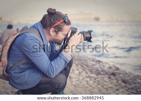 The bearded hipster photographer in blue jacket photographs on the banks of the Neva River in St. Petersburg.