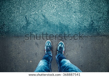 Alone man standing on textured grunge asphalt city street, point of view perspective. Pedestrian with blue shoes and jeans pants standing alone on grunge pavement. Blue color tone used. Royalty-Free Stock Photo #368887541