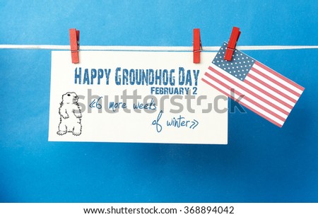 White envelope, cute face groundhog and text Happy Groundhog Day - 6 more weeks of winter. USA flag hanging on colorful pegs ( clothespin ) on a line against blue background. 