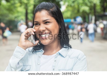 Native american woman speaking at phone in a park with trees and people in the background
