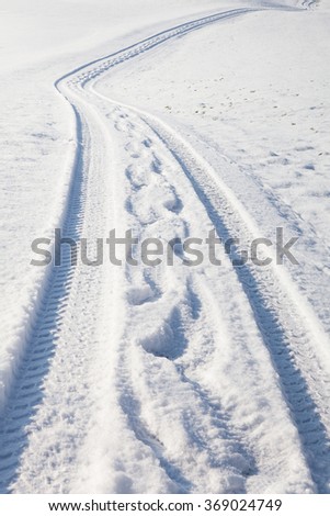 Car tire track and footprints on a empty winter road