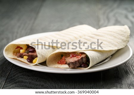 burritos with beef steak, corn, black beans and salsa sauce on wood table