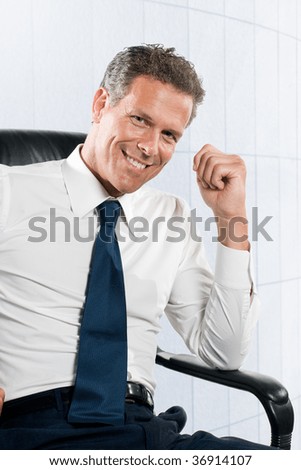 Smiling satisfied businessman looking at camera sit in his chair at office