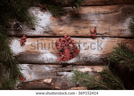 Red toy heart on wooden planks with spruce branches and red berries all around. Photo is made in vintage style. Perfect for making holiday atmosphere.
