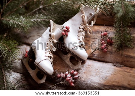 White old-fashioned skates on wooden planks with spruce branches and red berries all around. Photo is made in vintage style. Perfect for making holiday atmosphere.