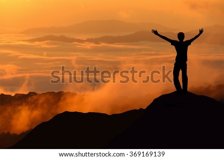 Silhouette of tourist man spread hand on top of a mountain enjoying morning mist at sunrise Royalty-Free Stock Photo #369169139