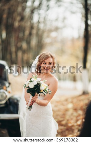 Fashion portrait of young bride with white dress with bouquet near retro car in autumn