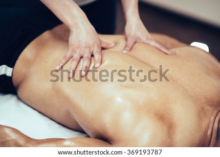 Back massage. Massage therapist massaging lower back region of a male athlete. Toned image Royalty-Free Stock Photo #369193787
