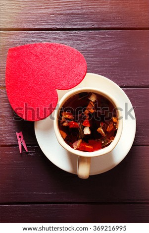 Cup of fruit tea on a limpet with red heart on wooden background closeup