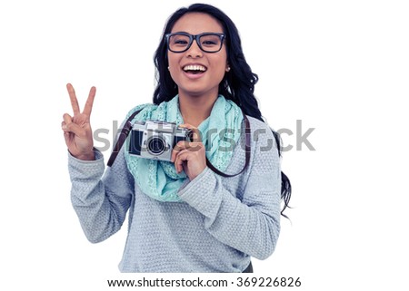 Asian woman holding digital camera and making peace sign with hand on white screen
