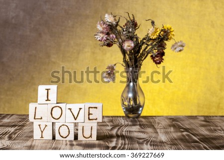 Wooden cubes with inscription "I LOVE YOU" and bouquet of dry flowers on new wooden board and burlap background. Selective focus.