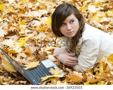 pretty girl lying on a carpet of autumn leaves with notebook