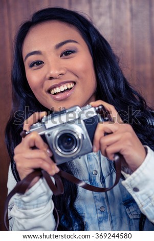 Asian woman holding digital camera against wooden wall