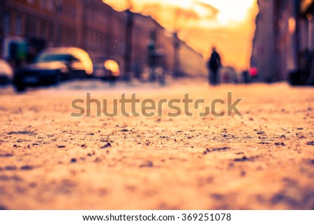 Bright winter sun in a big city, people go on snow-covered street. View from the sidewalk level, image in the orange-blue toning