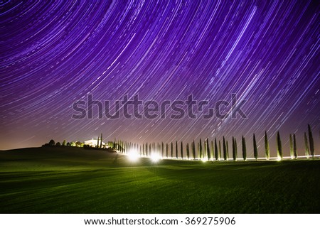 Beautiful Tuscany night landscape with star trails on the sky, cypresses and shining road in green meadow. Natural outdoor amazing fantasy background.