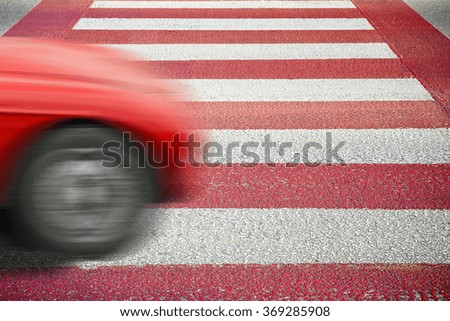Red and white pedestrian crossing with car on foreground.
