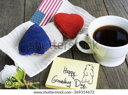 Heart shaped cookies color red, blue, white. Cup of coffee (tea), USA flag, decoration on old wooden table. Patriotic Breakfast Concept - cute face groundhog and text Happy Groundhog Day.