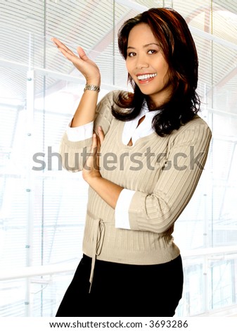 Happy Asian businesswoman in presenting gesture, in corporate interior as background.