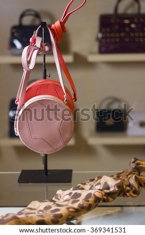 Two pink round small bags hanging on the stand in the shop window. Also on the table is a leopard scarf.
