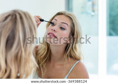 Smiling beautiful young woman putting on mascara in the bathroom mirror at home Royalty-Free Stock Photo #369388124
