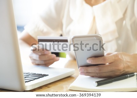 Woman using laptop and mobile phone to online shopping and pay by credit card. This picture is focus at woman's hand and use warm bright sunlight filter for feeling comfortable