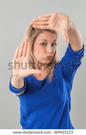 picture framing concept - pouting young blond woman making a frame with her hands for photographer, studio shot