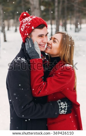 Young couple in love having fun in whiter forest in snow, embracing  and laughing . Wearing cozy warm clothes, knitted  hat and gloves . Young teen girl and her handsome boyfriend  dating.