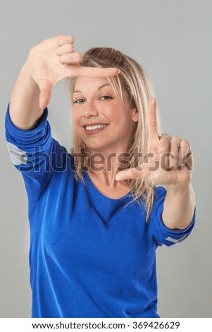 picture framing concept - smiling young blond woman making a frame with her fingers for photographer, studio shot