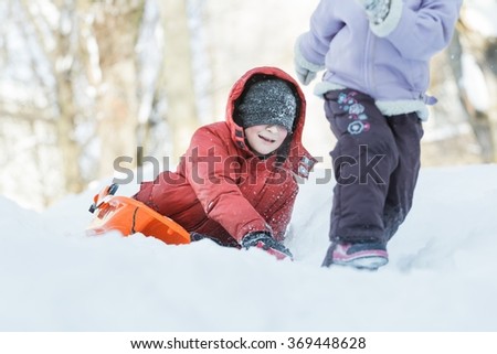 Exciting teenage boy chasing after his sibling sister outdoors on snow hill