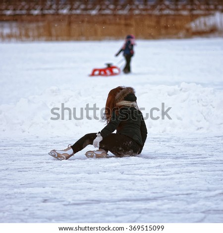 Girl falling down while ice skating on winter rink. Skating involves any sports or recreational activity which consists of traveling on surfaces or on ice using skates. Selective focus