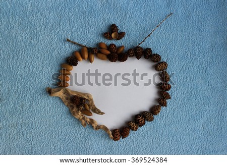 A heart frame of larch cones, acorns and dry sticks on a blue and white background.