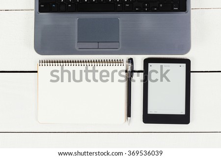 A gray laptop, black e-book, opened notebook with pen on white wooden table, point of view, mock-up, close up.