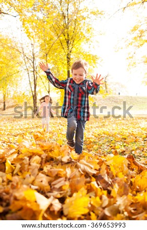 Image of beautiful boy jumping in the pile of autumn leaves, shallow depth of field